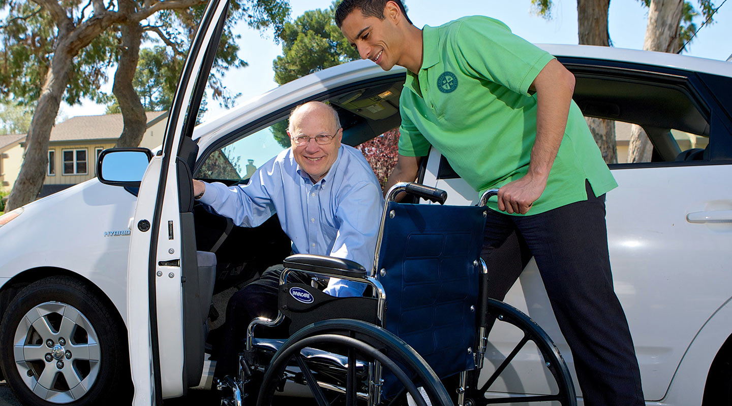 Occupational therapist helping disabled man get into a car